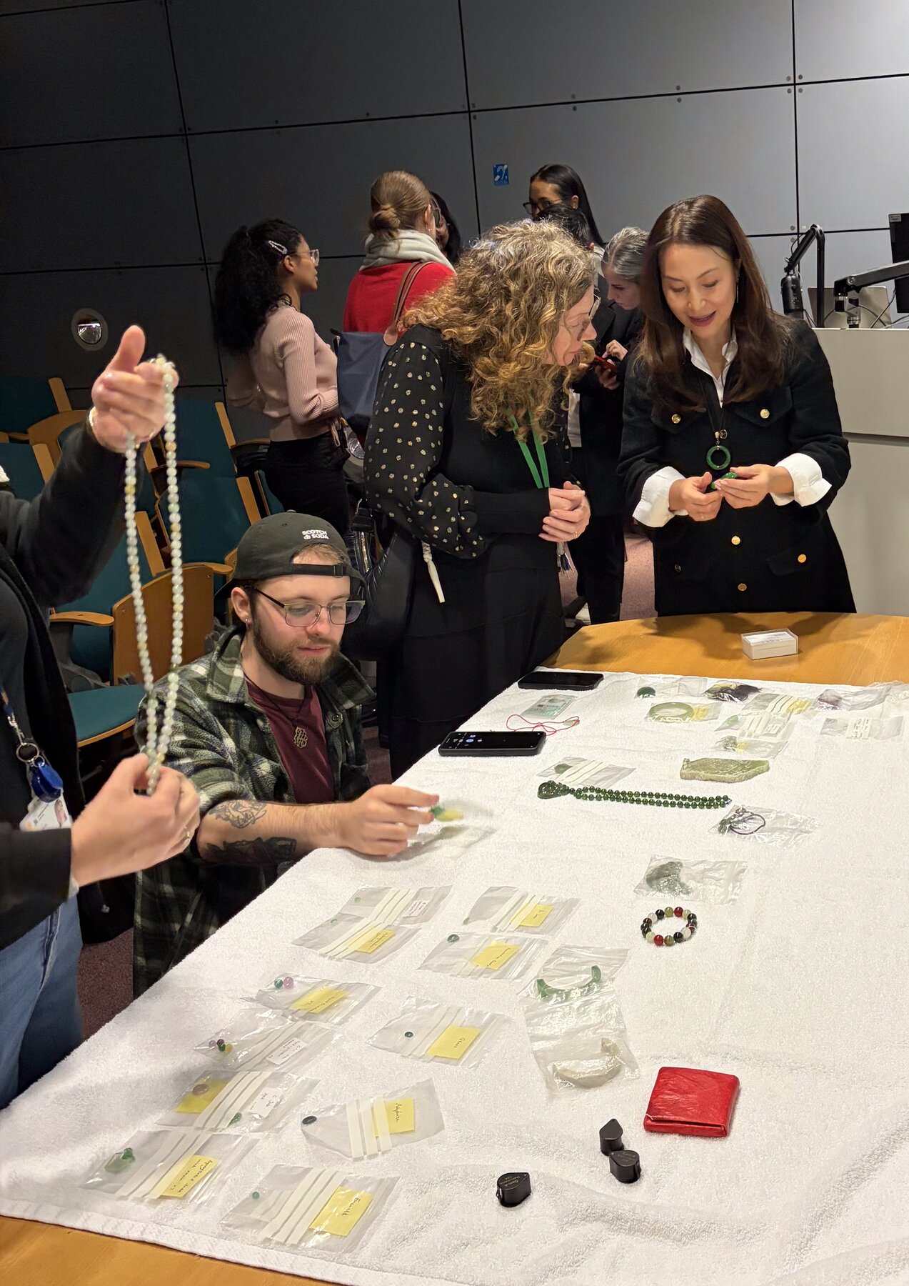Workshop wideshot: attendees examining jadeite pieces at the front of the room.